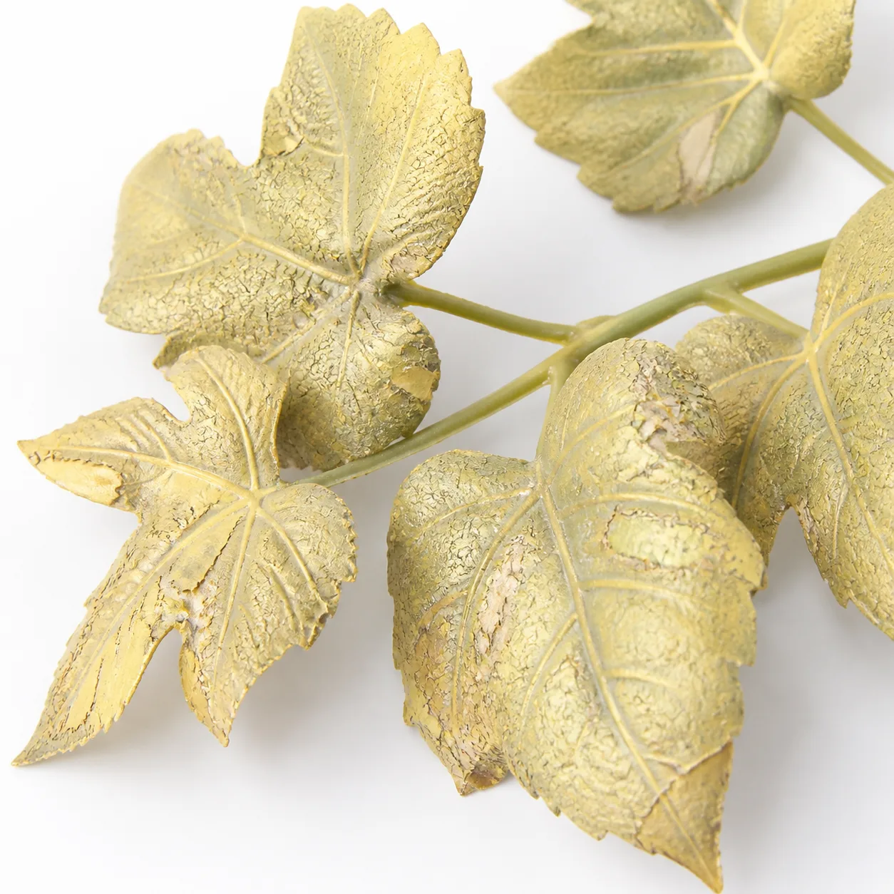 Close-up of UV-damaged standard plastic artificial plant leaves showing severe yellowing, surface cracking, and loss of structural integrity after sun exposure